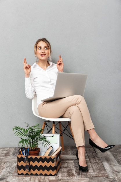 Ritratto di donna elegante utilizzando laptop mentre era seduto in poltrona con cose da ufficio, isolato