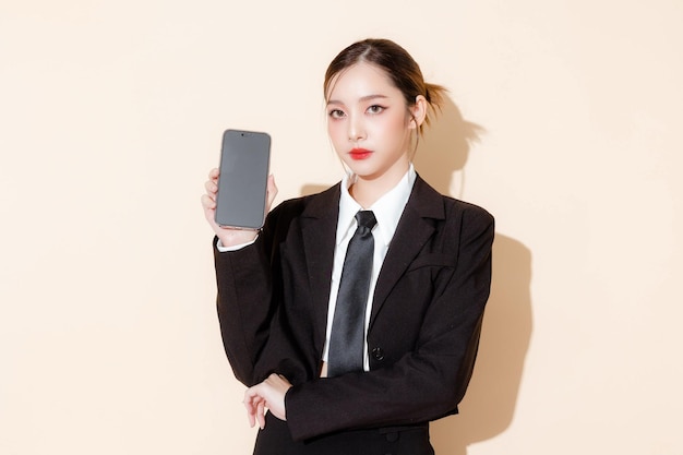 Ritratto di donna fiduciosa business manager che indossa elegante abito nero che mostra il cellulare con schermo vuoto isolato su sfondo beige Modello femminile in studio