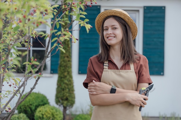 Ritratto di donna giardiniere che tiene le forbici da giardino in mano davanti alla casa del giardino