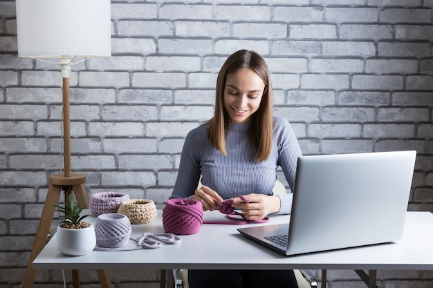 Ritratto di donna graziosa che impara a lavorare a maglia a casa. Insegnare a lavorare a maglia online.