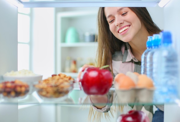 Ritratto di donna in piedi vicino al frigorifero aperto pieno di frutta e verdura di cibo sano