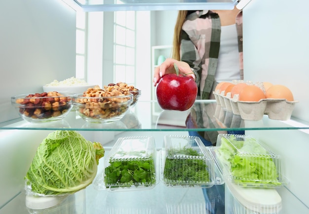 Ritratto di donna in piedi vicino al frigorifero aperto pieno di frutta e verdura di cibo sano