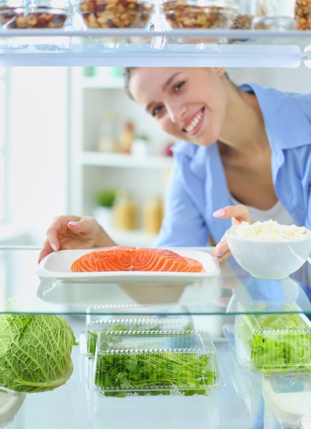 Ritratto di donna in piedi vicino al frigorifero aperto pieno di frutta e verdura di cibo sano