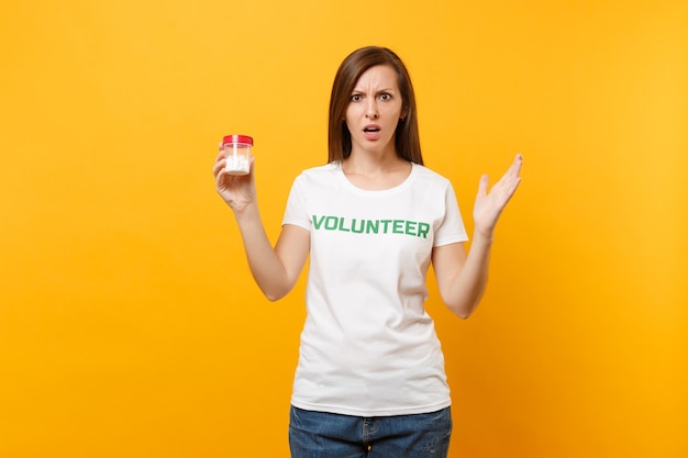 Ritratto di donna in t-shirt bianca scritta iscrizione titolo verde volontario che tiene bottiglia con pillole farmaco isolato su sfondo giallo. Aiuto volontario di assistenza gratuita, concetto di salute di grazia di carità.