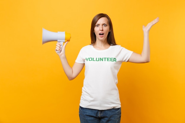 Ritratto di donna in t-shirt bianca scritta iscrizione verde titolo volontario urlare in megafono discorso pubblico isolato su sfondo giallo. Aiuto volontario gratuito di assistenza, concetto di lavoro di grazia di carità.