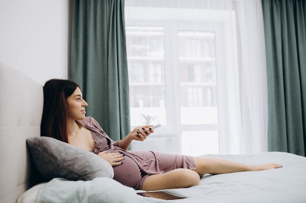 Ritratto di donna incinta carina che guarda la televisione a casa