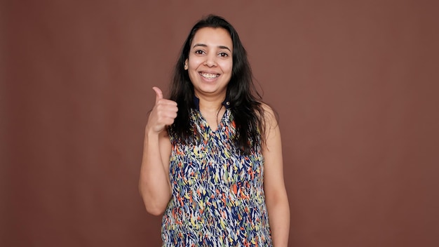 Ritratto di donna indiana che fa il pollice in alto gesto sulla fotocamera, dando like e approvazione all'idea. Raffreddare simbolo ok ottimista con soddisfazione e positività, accordo di successo.