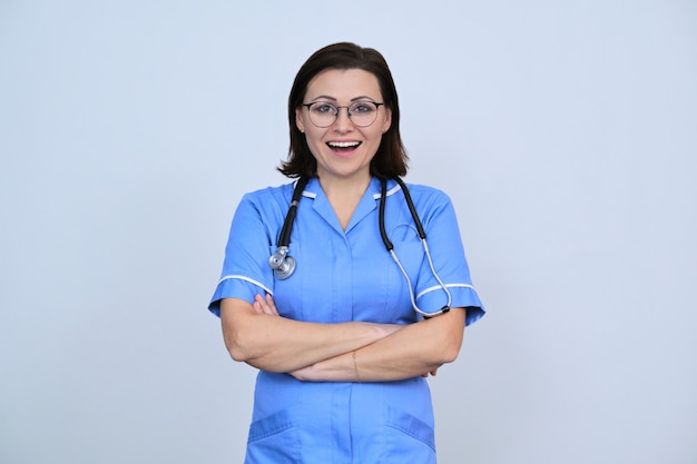 Ritratto di donna infermiera in uniforme blu con le braccia incrociate, lavoratore medico positivo fiducioso che guarda l'obbiettivo, grigio