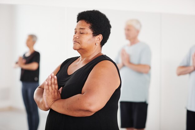 Ritratto di donna matura africana che medita con gli occhi chiusi durante la lezione di yoga con altri anziani...