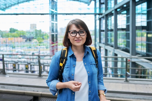 Ritratto di donna matura alla stazione ferroviaria femminile con zaino che guarda l'obbiettivo