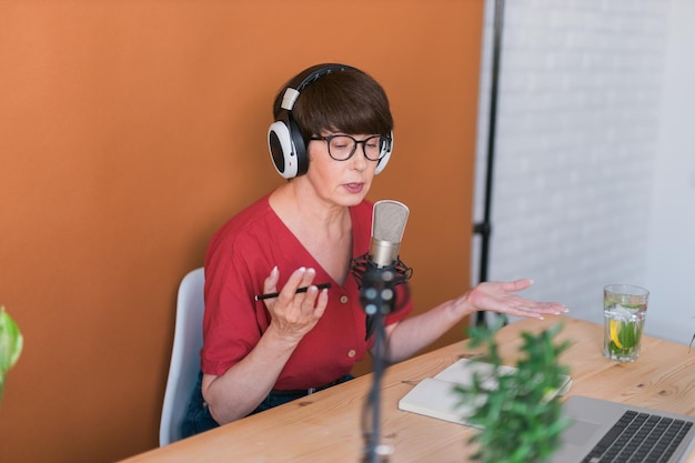 Ritratto di donna matura che indossa le cuffie e parla al podcast della stazione radio online e al concetto di trasmissione