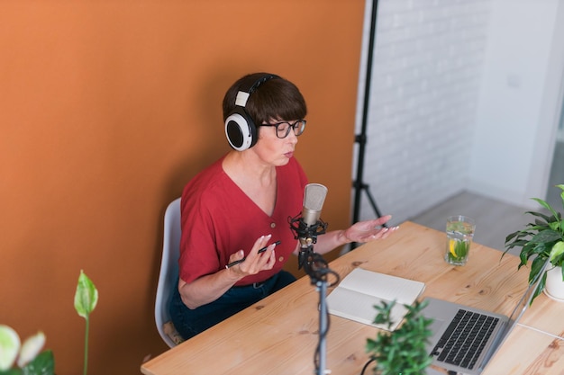 Ritratto di donna matura che indossa le cuffie e parla al podcast della stazione radio online e al concetto di trasmissione