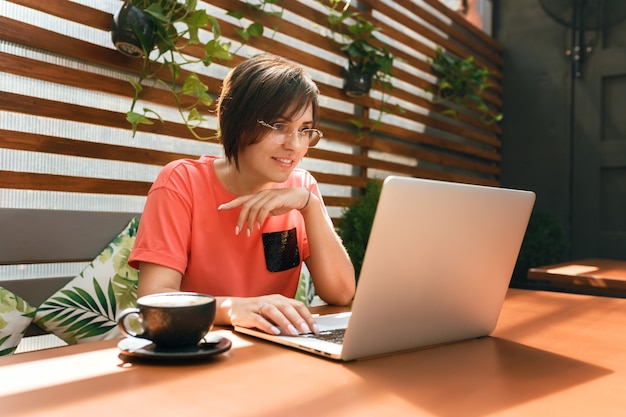 ritratto di donna matura e sicura di sé che si siede sulla terrazza estiva al bar utilizzando laptop