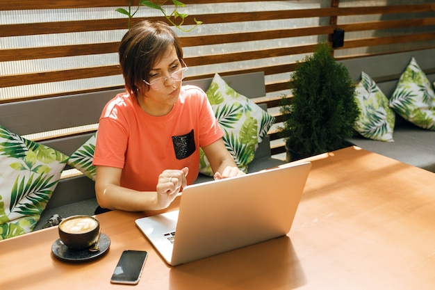 ritratto di donna matura e sicura di sé che si siede sulla terrazza estiva al bar utilizzando laptop