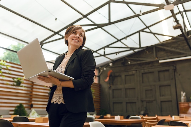 ritratto di donna matura e sicura di sé che si siede sulla terrazza estiva al bar utilizzando laptop