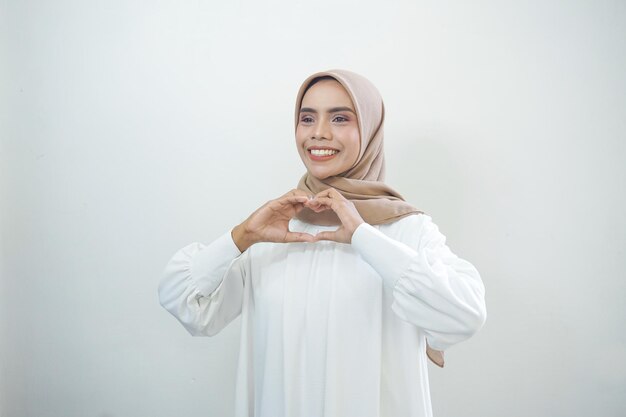 Ritratto di donna musulmana asiatica sorridente che mostra il gesto del cuore isolato su sfondo bianco