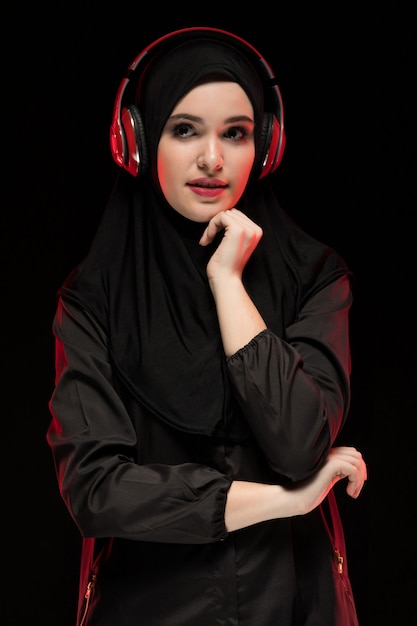 Ritratto di donna musulmana che indossa l'hijab nero ascoltando musica in cuffia