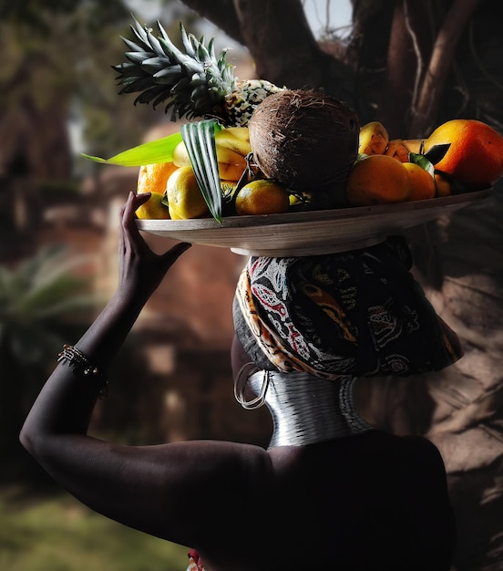 ritratto di donna nera africana con piatto di frutta in testa su sfondo tropicale