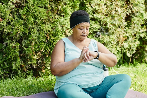 Ritratto di donna nera matura che guarda lo smartwatch mentre si fa una pausa durante l'allenamento all'aperto