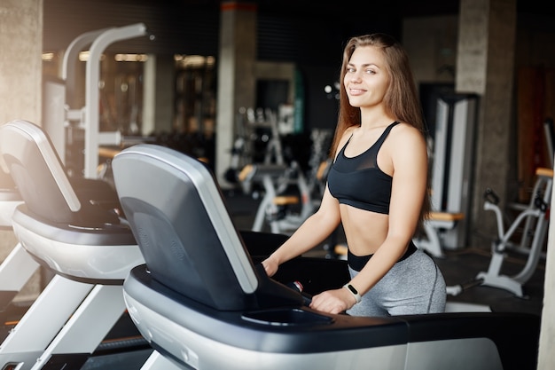 Ritratto di donna pazza in forma su un mulino a filo sorridente. Preparatore atletico in fase di riscaldamento la mattina presto in palestra vuota.