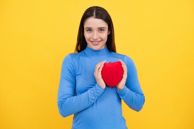 Ritratto di donna piuttosto sorridente che tiene il cuore di carta nelle sue mani su sfondo giallo Concetto di amore