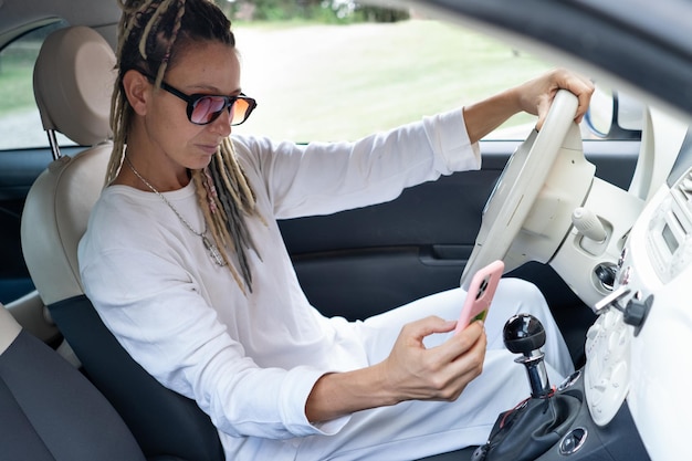 Ritratto di donna rasta in macchina che controlla il suo telefono