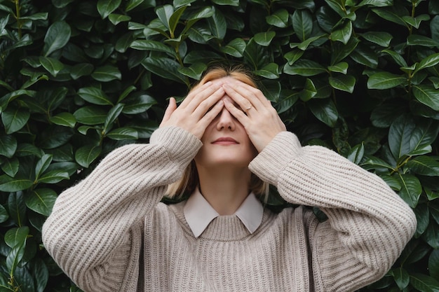 Ritratto di donna rilassata con gli occhi chiusi sullo sfondo di un muro di foglie verdi Concetto di fuori ufficio WorkLifeBalance Prendersi una pausa Zen ed equilibrare le persone Stabilità attraverso la salute mentale