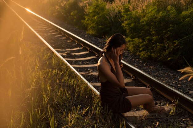 Ritratto di donna seduta su una ferrovia nei raggi del tramonto.