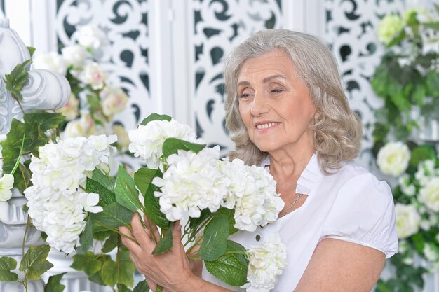 Ritratto di donna senior felice che posa con i fiori a casa