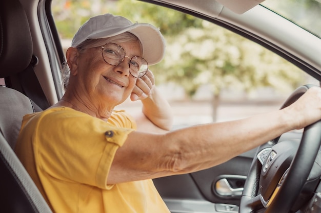 Ritratto di donna senior rilassata che tiene il volante dell'auto guardando la fotocamera durante il viaggio in auto