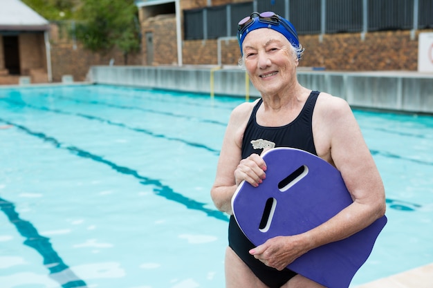 Ritratto di donna senior sorridente holding kickboard a bordo piscina