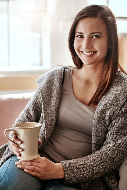 Ritratto di donna sorridente e caffè a casa su un divano del soggiorno che si sente calmo e rilassato Tè della casa e felicità mattutina di una persona con un drink su un divano del salotto tranquillo e sorridente da solo