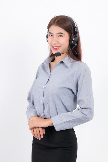 Ritratto di donna sorridente felice assistenza clienti operatore telefonico capelli corti, indossa una camicia bianca con auricolare in piedi un lato tenendo l'auricolare isolato su superficie bianca