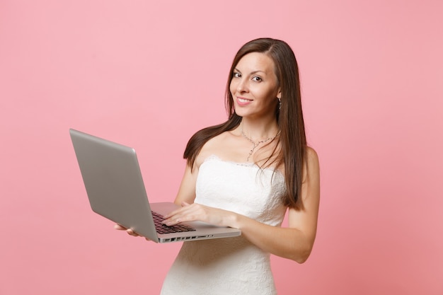 Ritratto di donna sorridente in abito bianco, lavorando su computer pc portatile