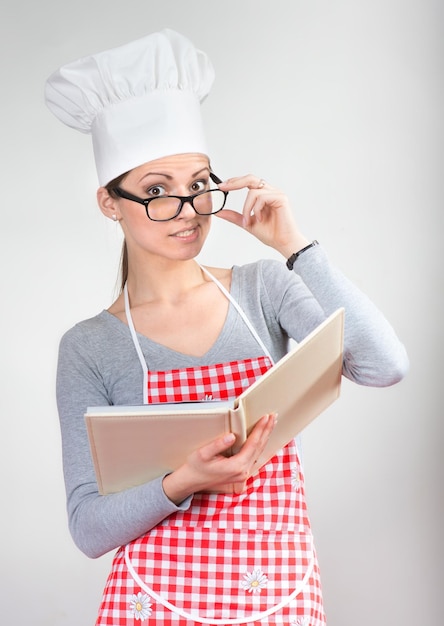 Ritratto di donna sorridente in capo cappello con il libro di cucina che alza il dito indice
