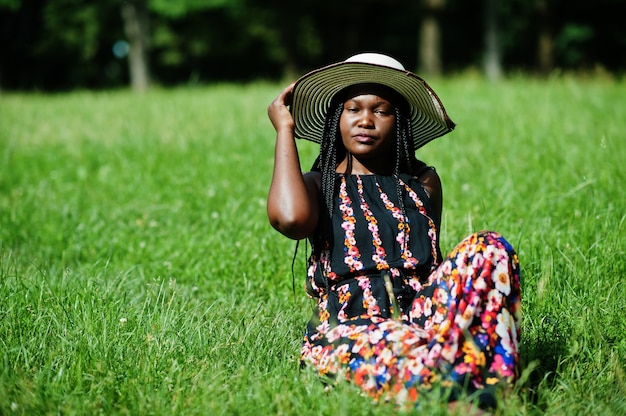 Ritratto di donna splendida in cappello estivo seduto all'erba verde nel parco