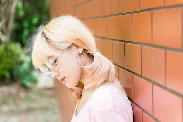 Ritratto di donna tailandese capelli dorati in stile giappone su muro di mattoni arancioni Ragazza asiatica posa per scattare una foto all'aperto