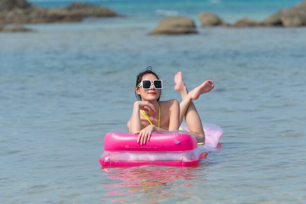 Ritratto di donna tailandese in bikini su un gonfiabile rosa sull'acqua in spiaggia