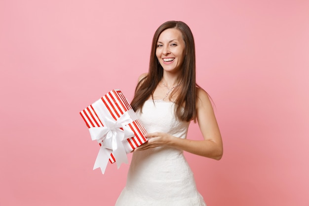 Ritratto di donna tenera sorridente in bellissimo abito bianco che tiene in mano una scatola rossa con un regalo regalo