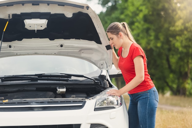 Ritratto di donna triste che guarda il motore dell'auto rotta e aspetta aiuto