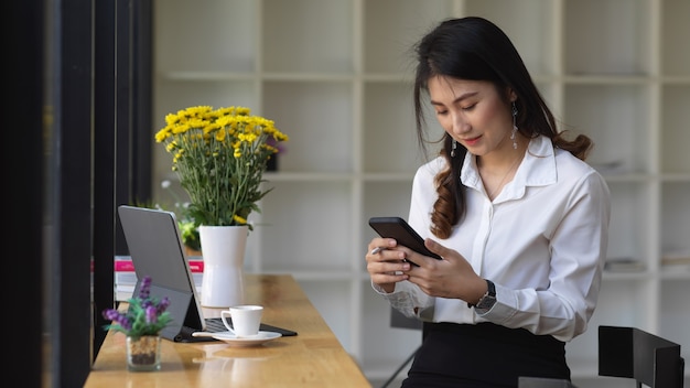 Ritratto di donna utilizza lo smartphone mentre è seduto nella caffetteria con tavoletta digitale e forniture