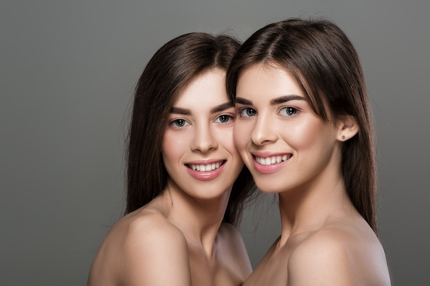 Ritratto di donne gemelle sorridenti con pelle perfetta e trucco naturale e capelli lunghi. moda