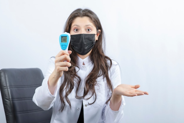 Ritratto di dottoressa in maschera medica e termometro con camice bianco.