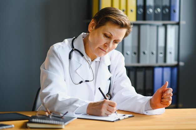 Ritratto di dottoressa matura in camice bianco sul posto di lavoro