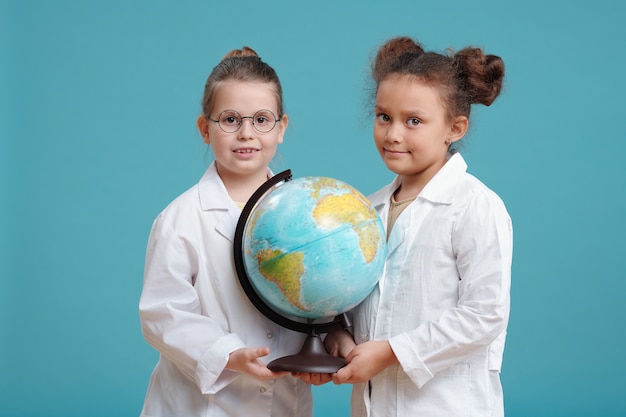 Ritratto di due bambine che tengono un grande globo mondiale e sorridono alla telecamera sullo sfondo blu