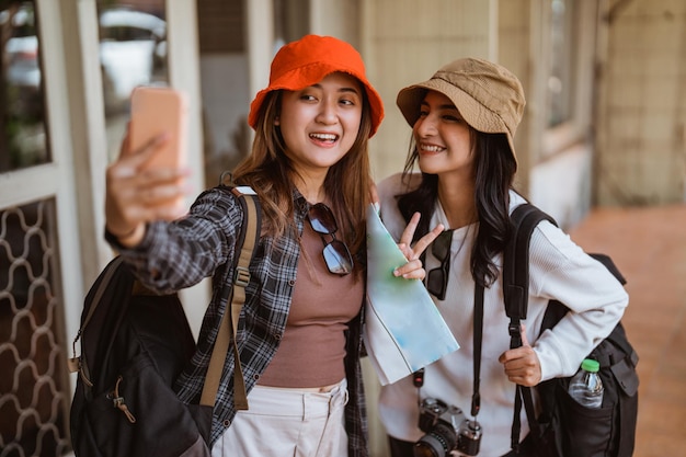 Ritratto di due bellissimi turisti locali che fanno selfie usando una telecamera di cellulare con una casa nel