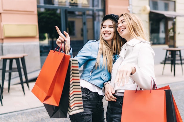 Ritratto di due bionde in mezzo alla strada dello shopping, una di loro indica i discount