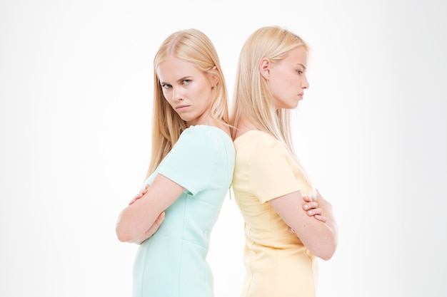 Ritratto di due donne arrabbiate in piedi l'una di fronte all'altra con le braccia incrociate isolate su un muro bianco
