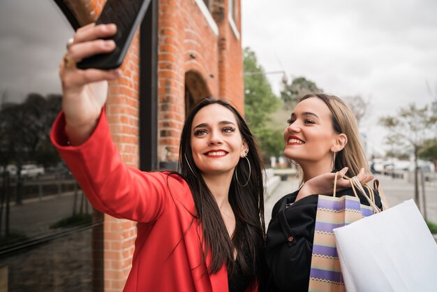 Ritratto di due giovani amici che godono di fare shopping insieme mentre si prende un selfie con il telefono in strada