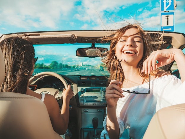 Ritratto di due giovani belle e sorridenti donne hipster in auto decappottabile